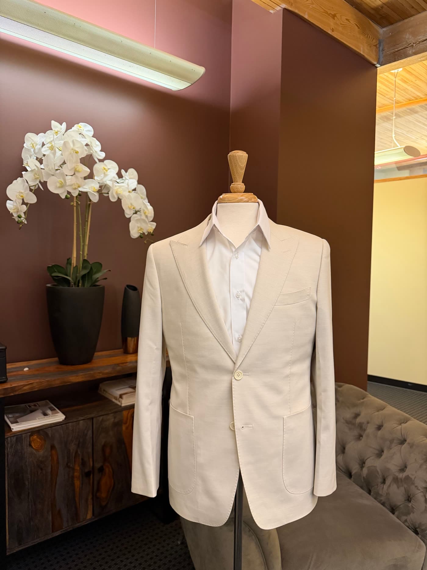 A cream custom dinner jacket on a form beside white orchids