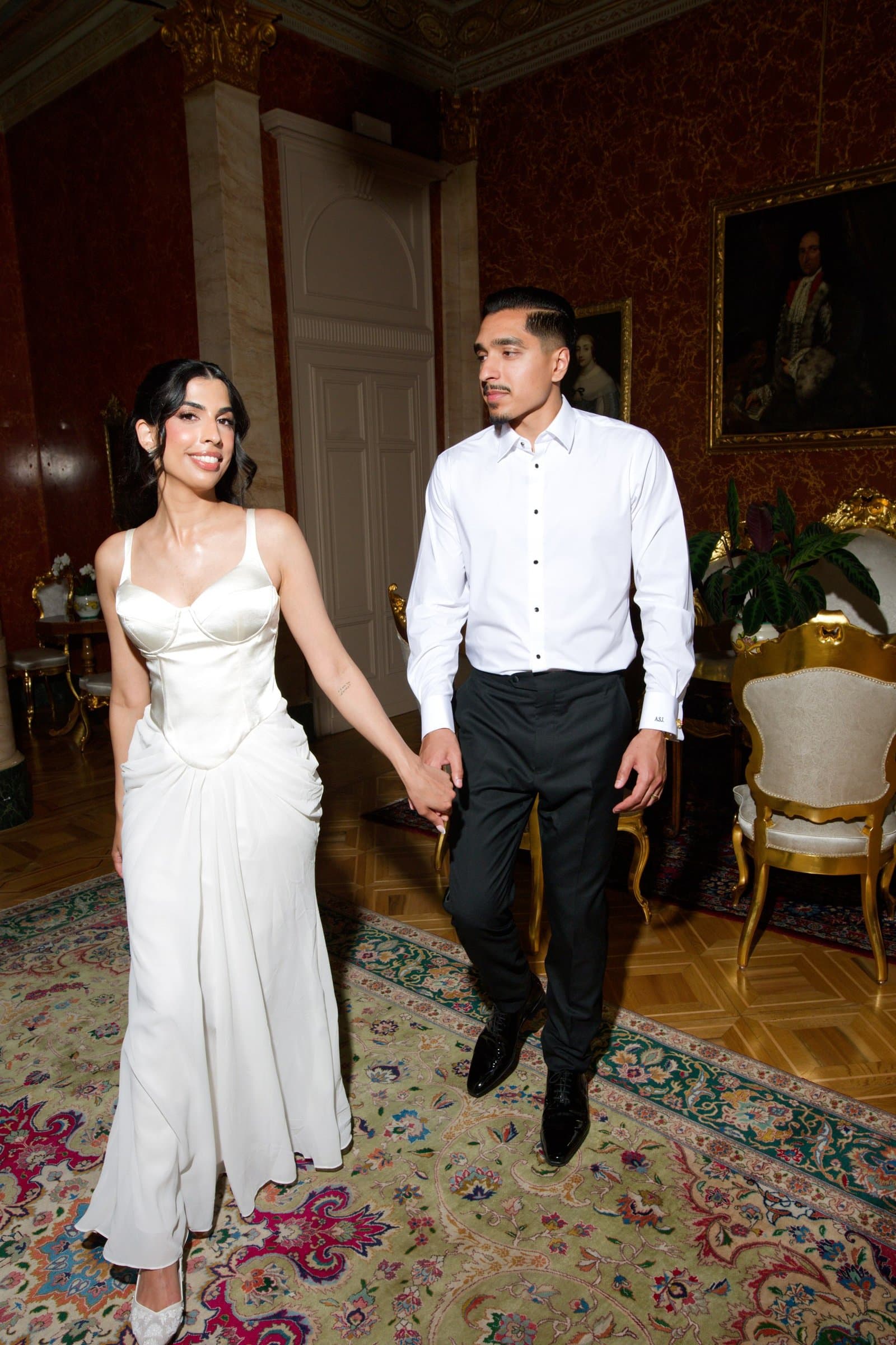 The couple in white and black, hand in hand, crossing a red villa salon