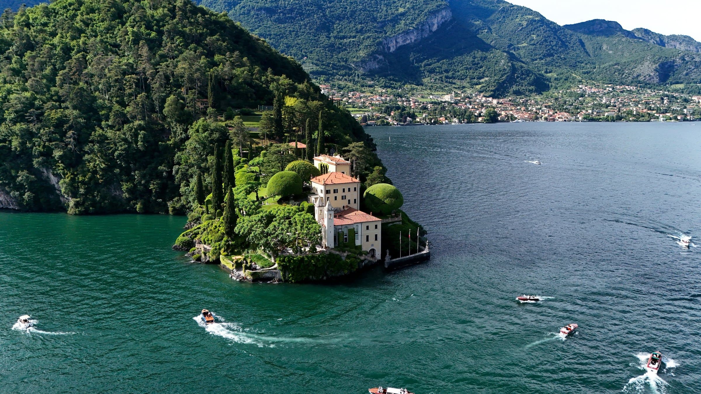 A villa on a wooded point of Lake Como, boats crossing the water below