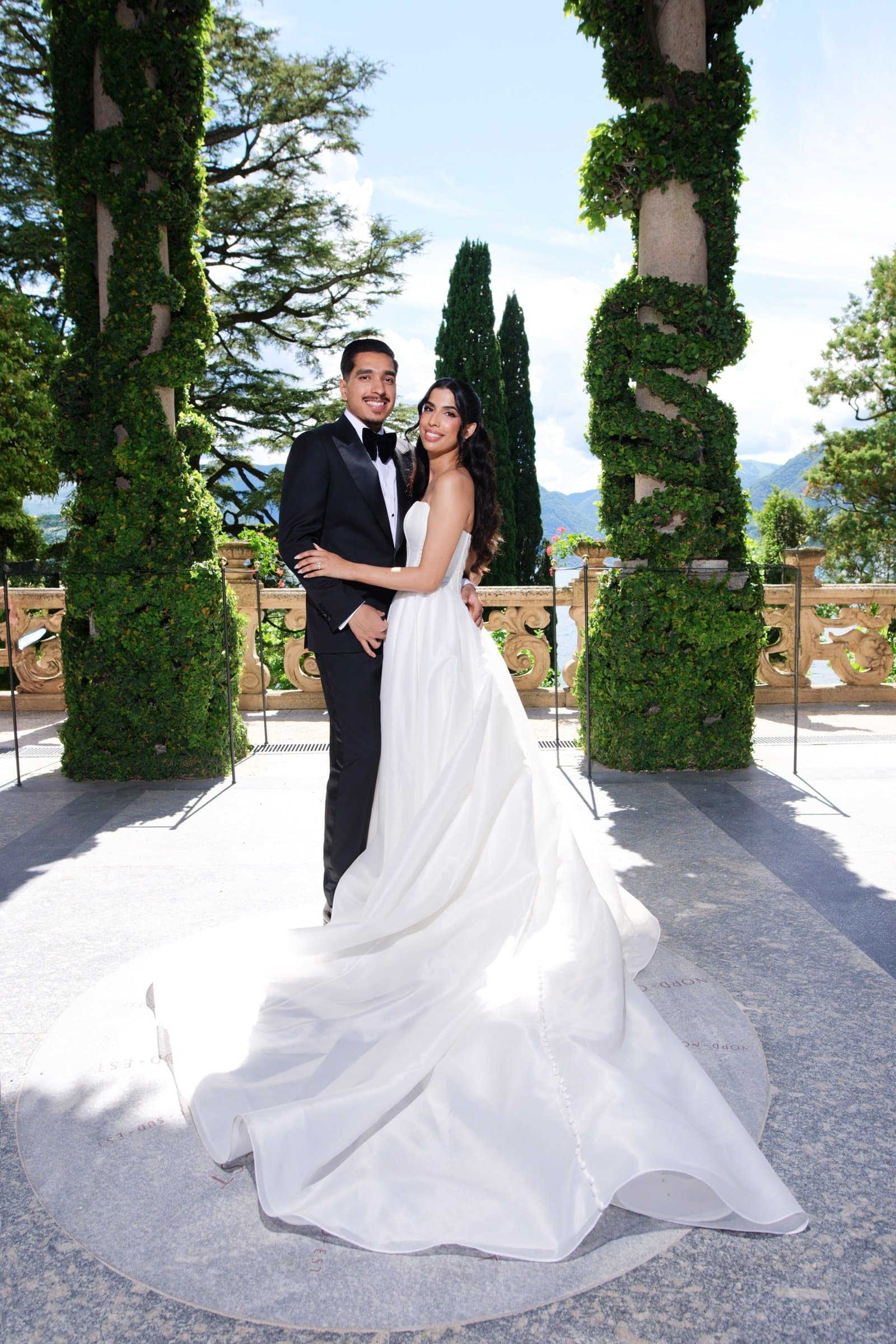 The bride and groom between two spiral topiaries on a terrace above Lake Como