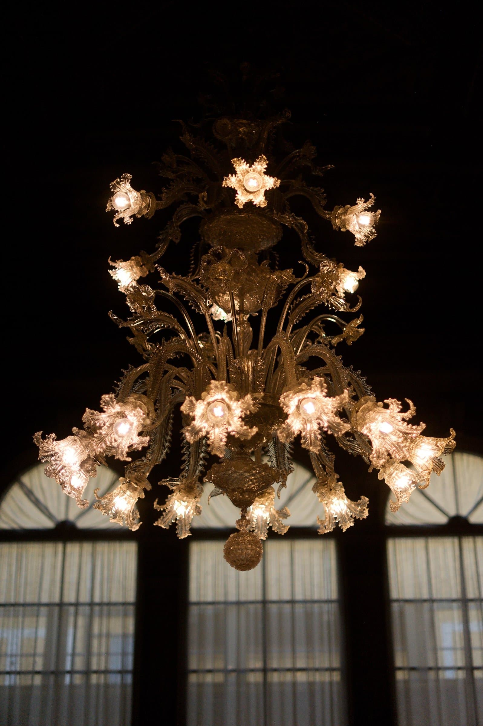 A glass chandelier lit against tall windows at night