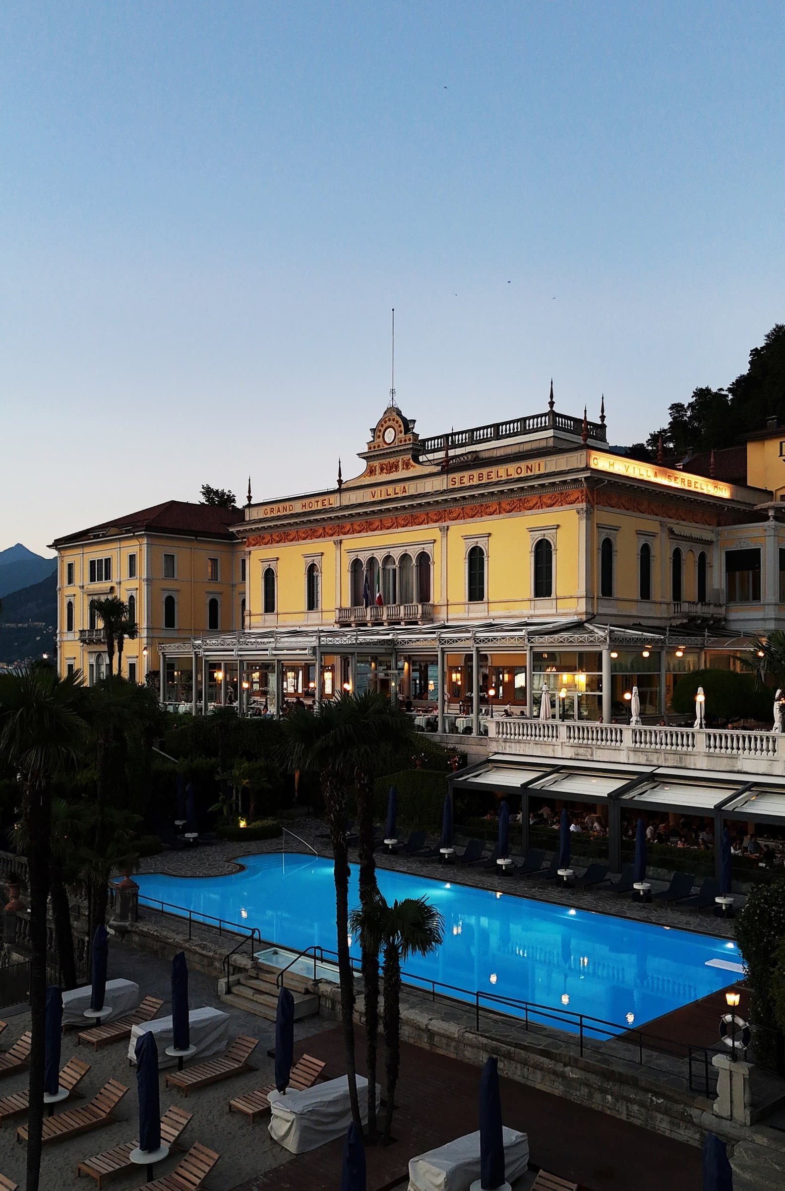 A grand hotel and its pool on the shore of Lake Como at dusk