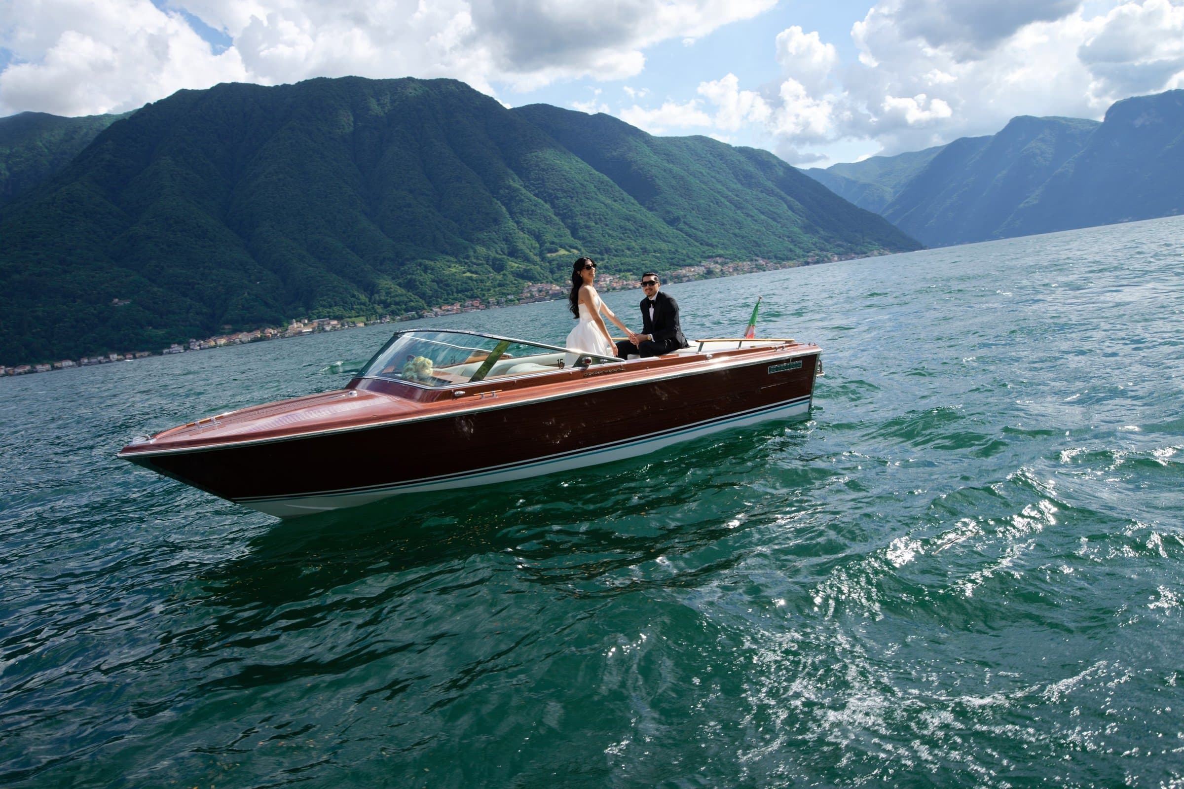 The bride and groom crossing Lake Como in a wooden Riva, the mountains behind