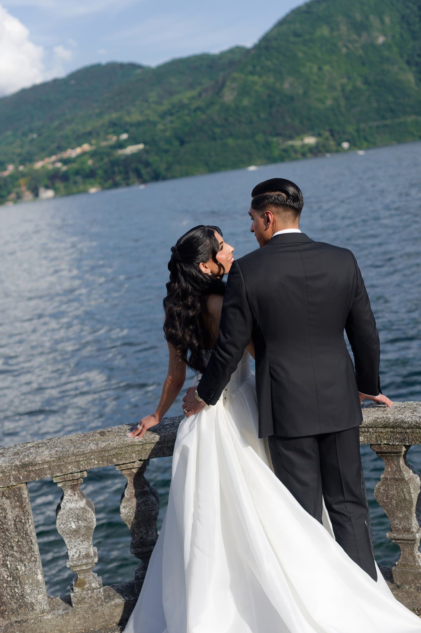 The bride and groom at a stone balustrade above Lake Como, seen from behind