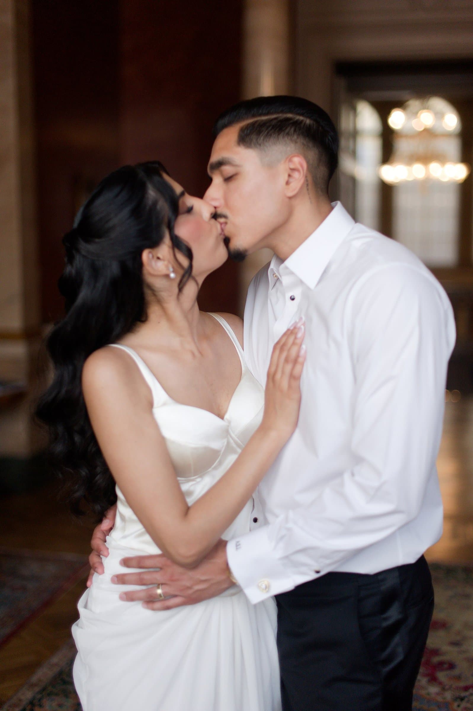 The couple kissing in a villa salon lit by a chandelier