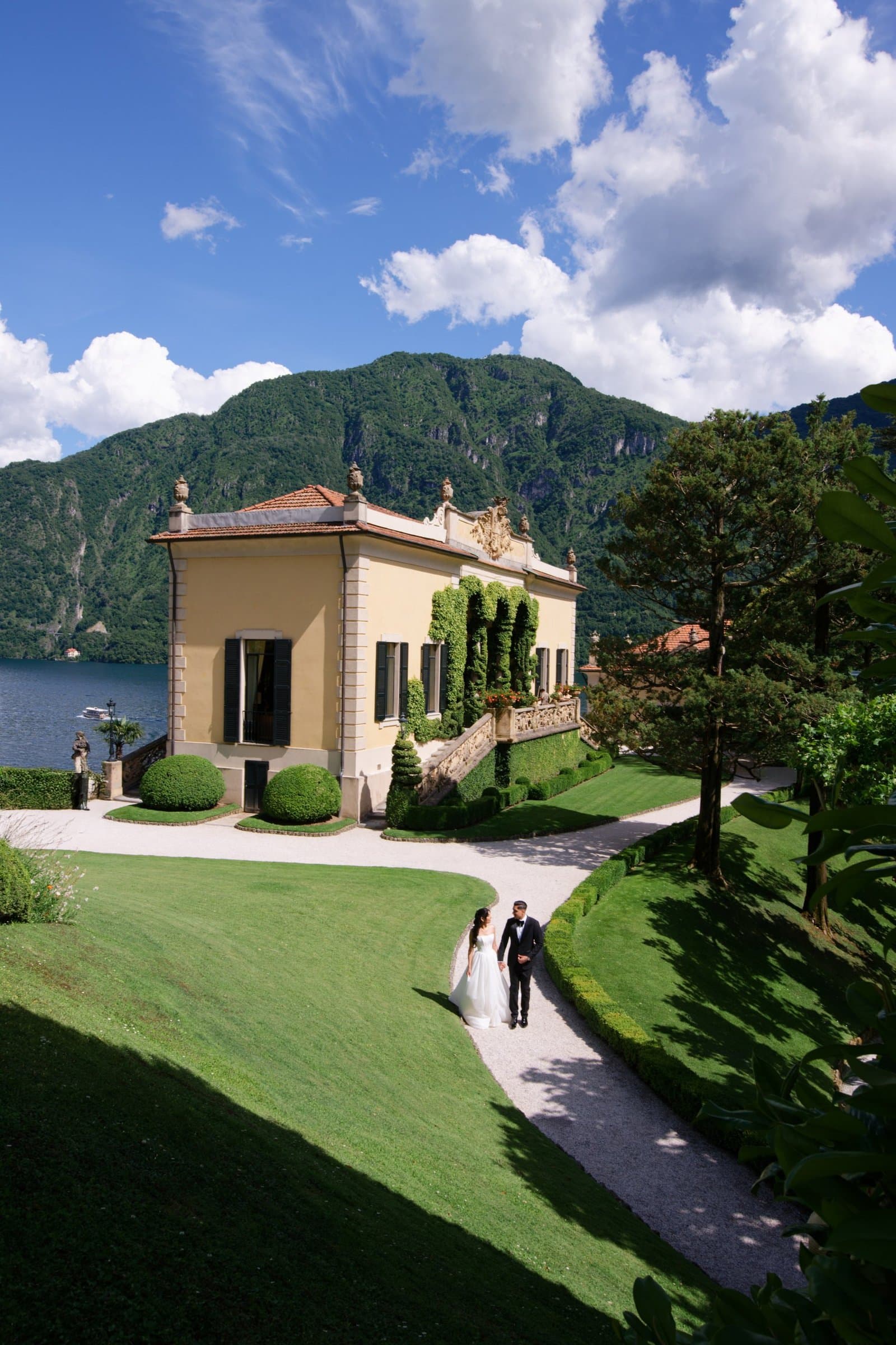 The bride and groom on a curving garden path below a lakeside villa