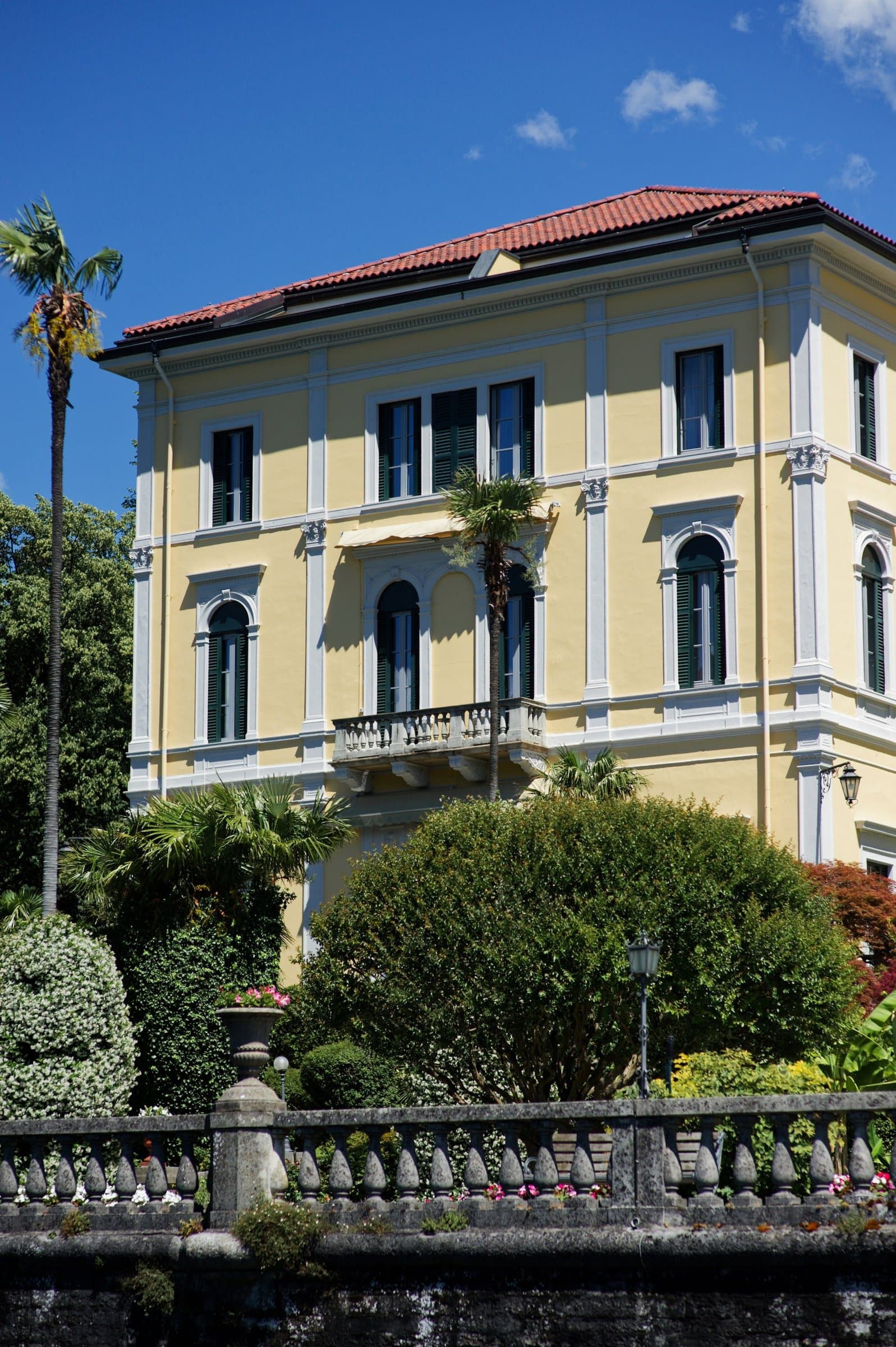 A yellow villa with green shutters behind a stone balustrade
