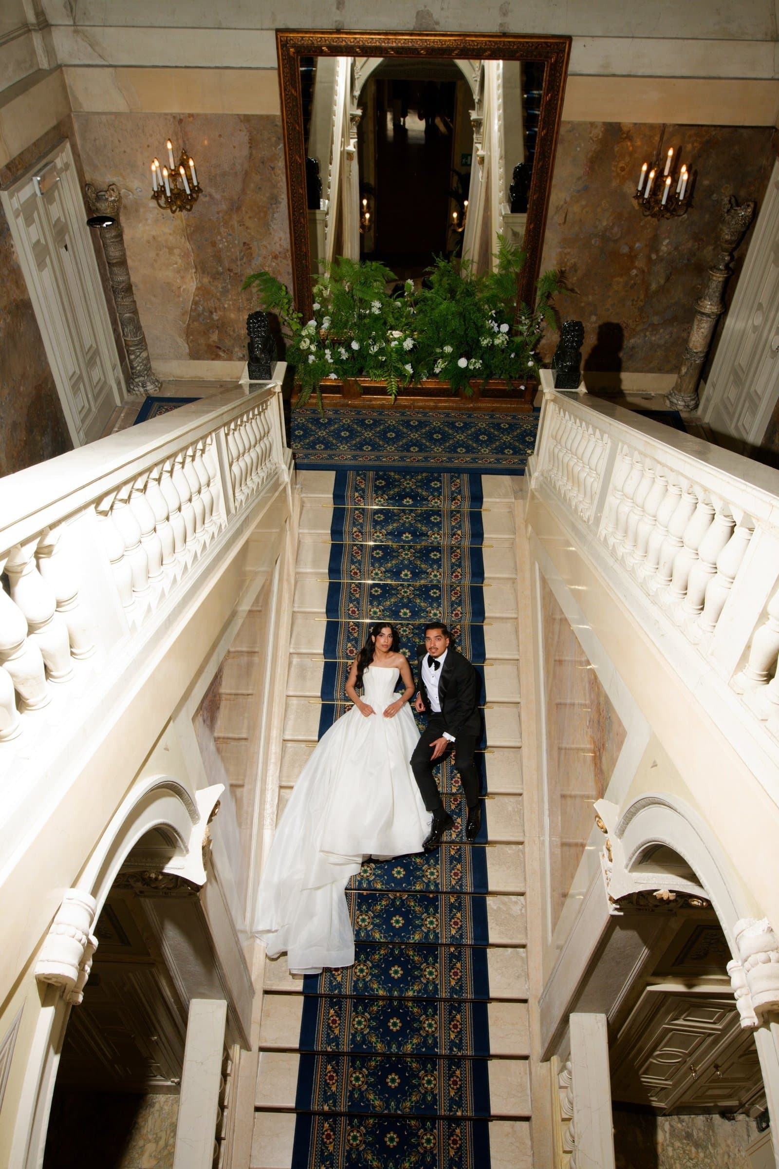 The bride and groom on a carpeted marble staircase, seen from the landing above