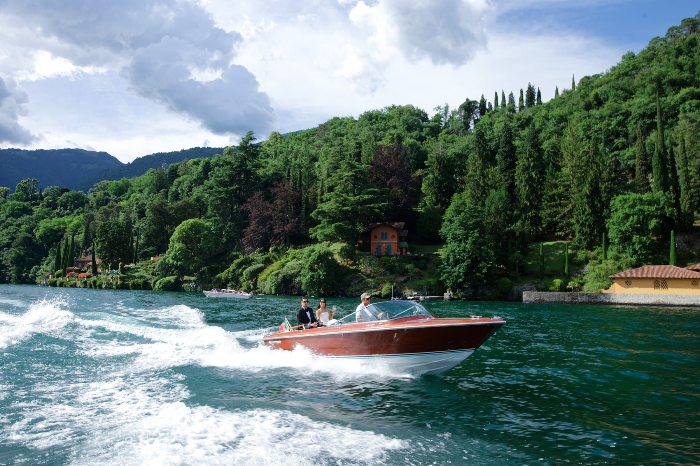 A wooden Riva speedboat crossing Lake Como below wooded hills