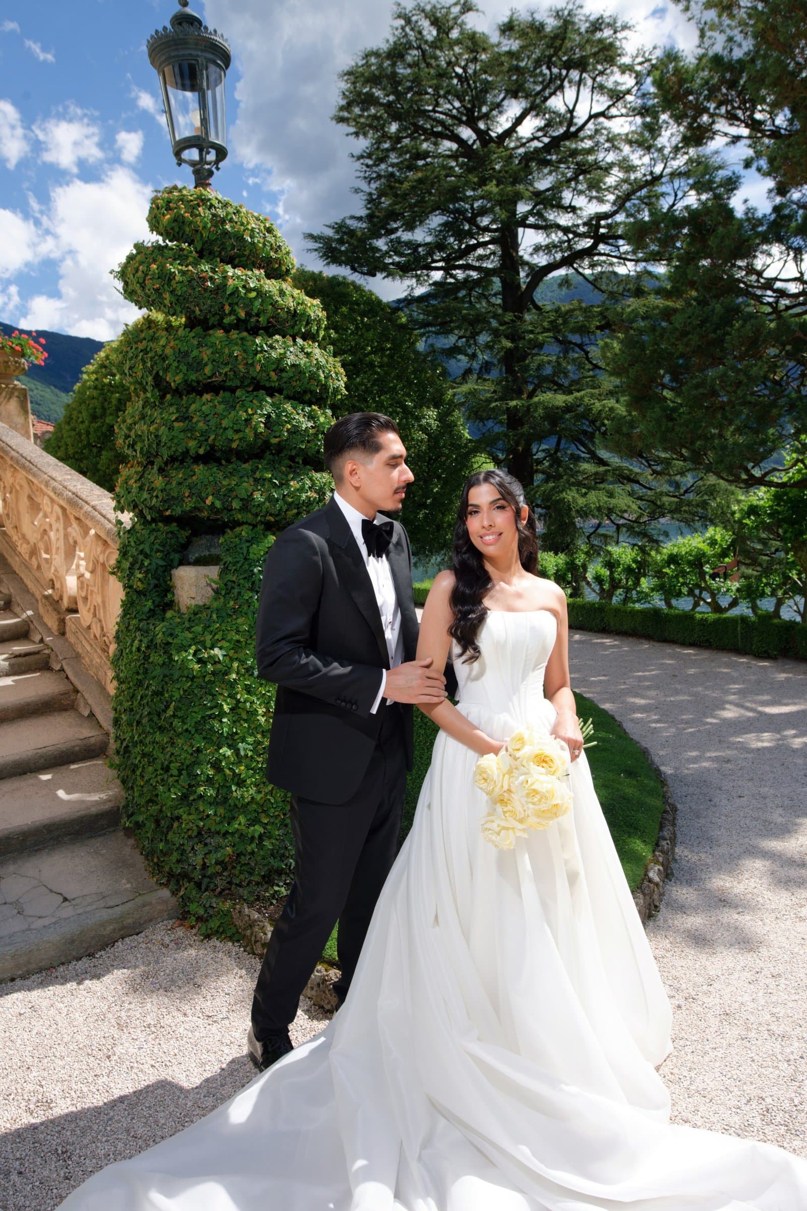 The bride and groom beside a spiral topiary on a villa garden path