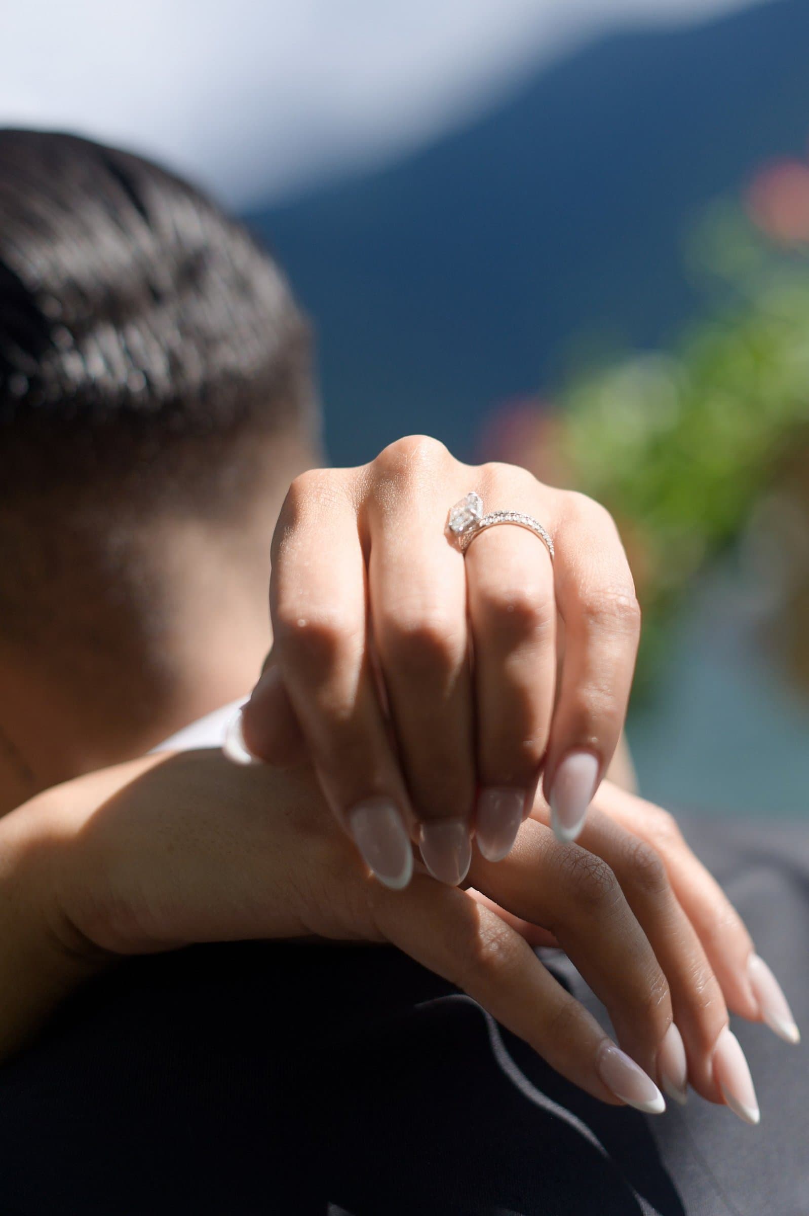 The bride's hand, with her engagement ring, resting on the groom's tuxedo shoulder