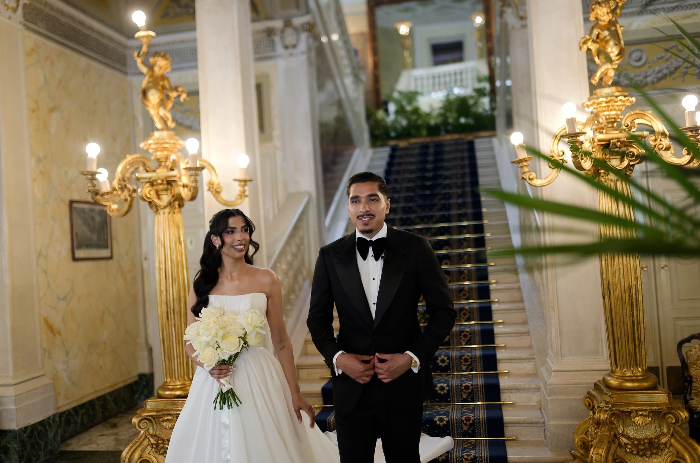 The bride and groom in a gilded hotel hall at the foot of a carpeted marble staircase