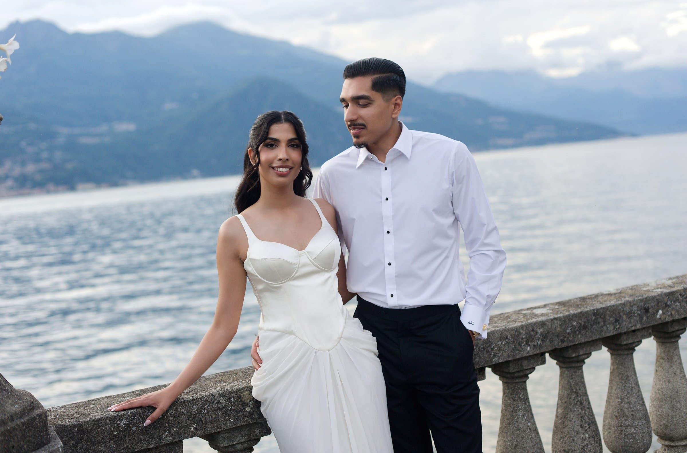 The couple at a stone balustrade above Lake Como, she in white silk, he in a white shirt