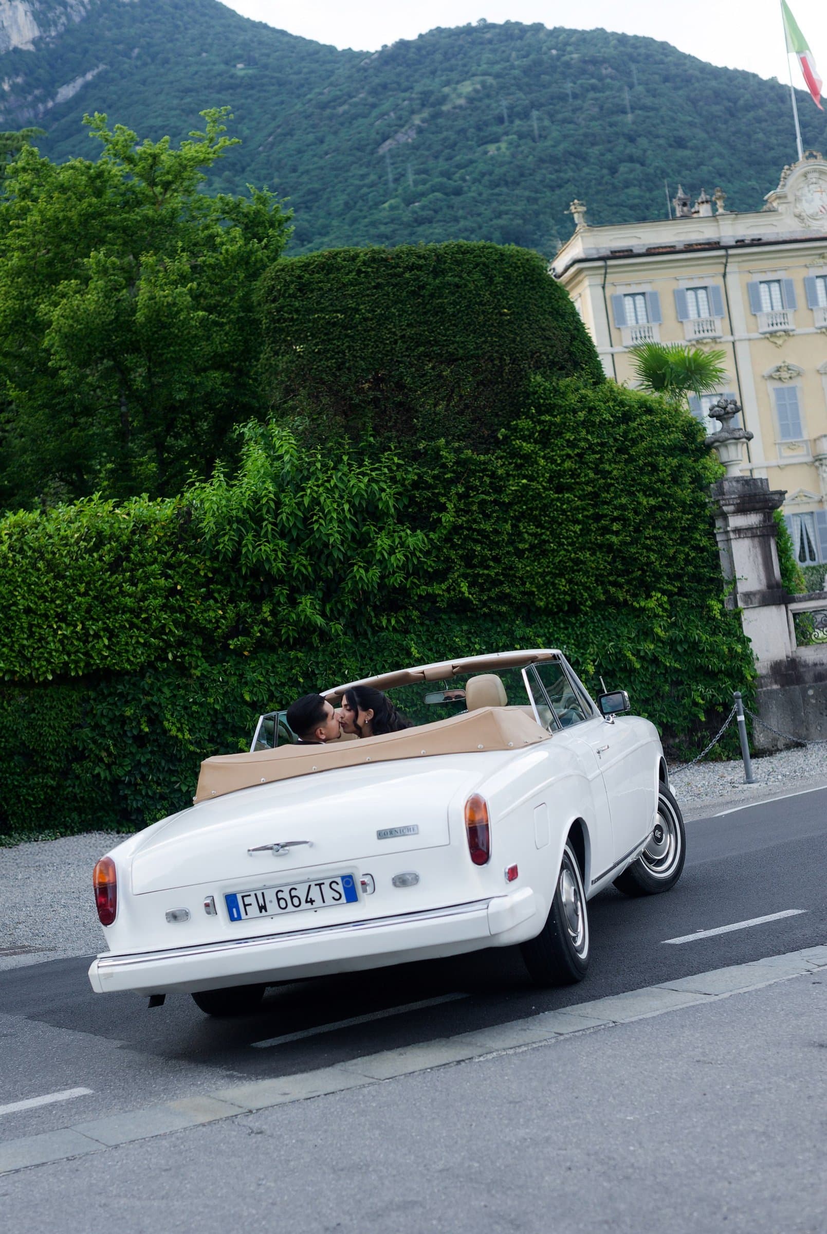 A white Rolls-Royce convertible pulling away from a villa on Lake Como