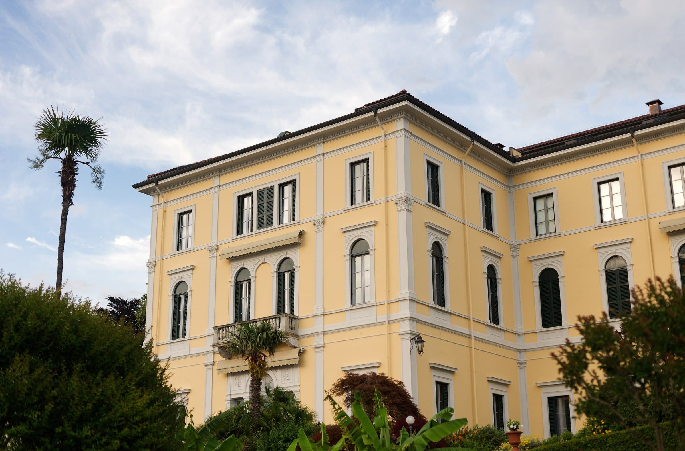 A yellow lakeside villa and a palm tree under a summer sky