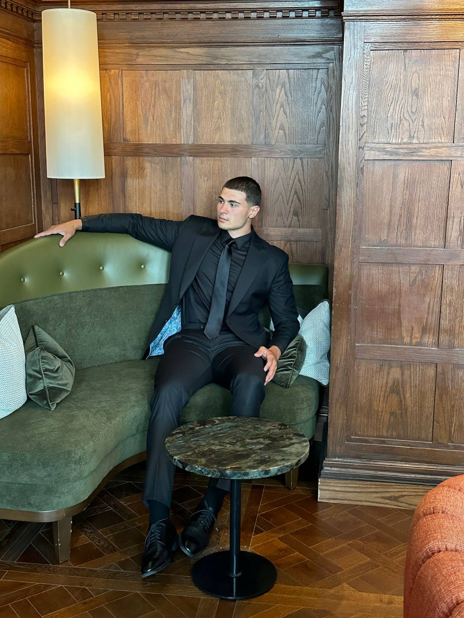 A custom all-black business suit by Conxeppt in Edmonton, worn on a green velvet banquette