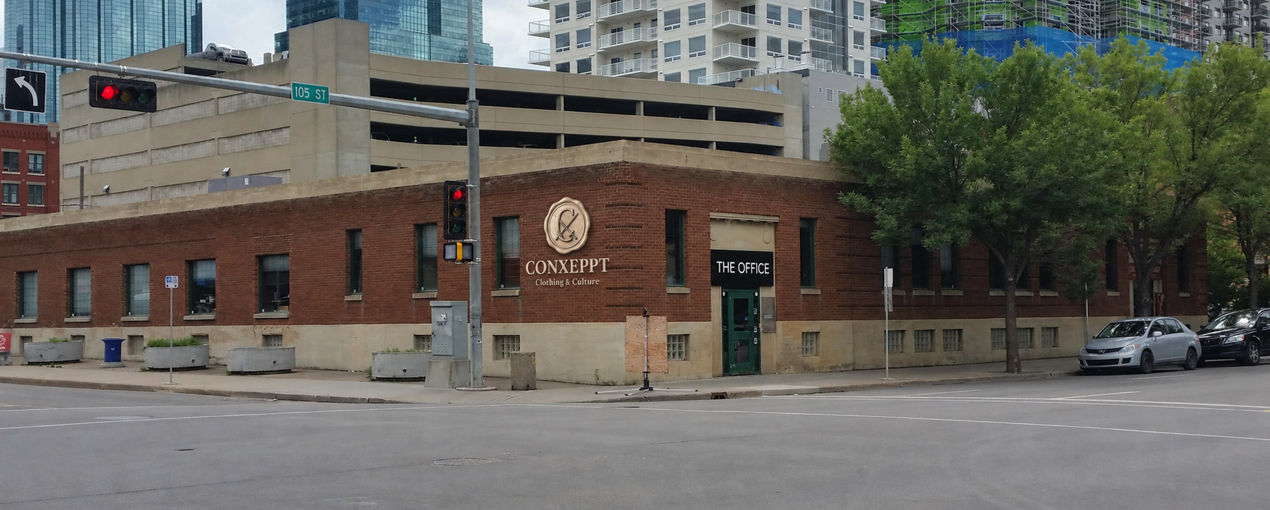 THE OFFICE sign above the green entrance door, with a Conxeppt wax-seal signage mockup on the red brick wall