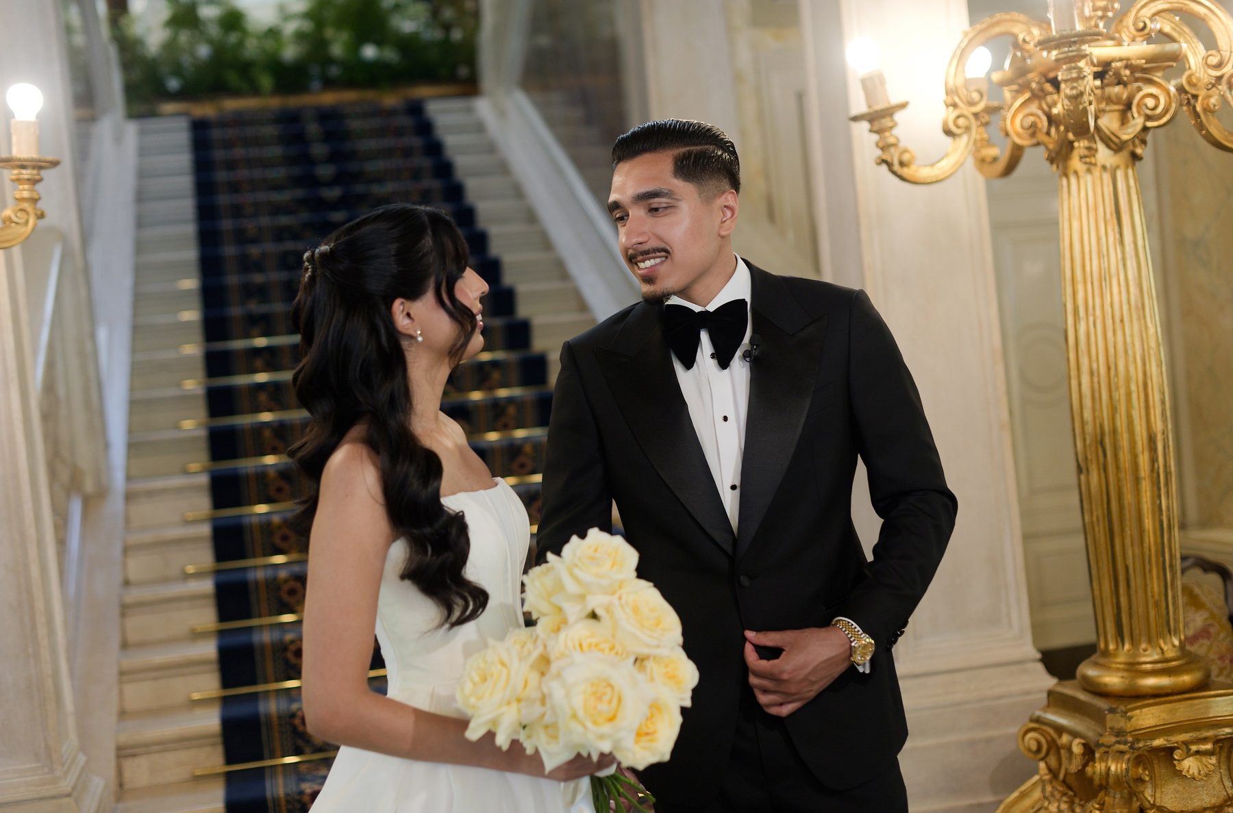 The couple on the villa staircase, the bride holding white roses