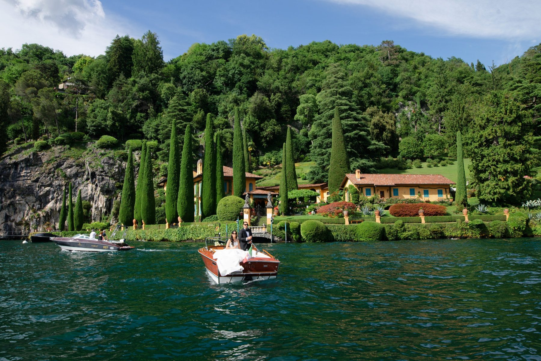 A Riva passing a lakeside villa and its cypress gardens