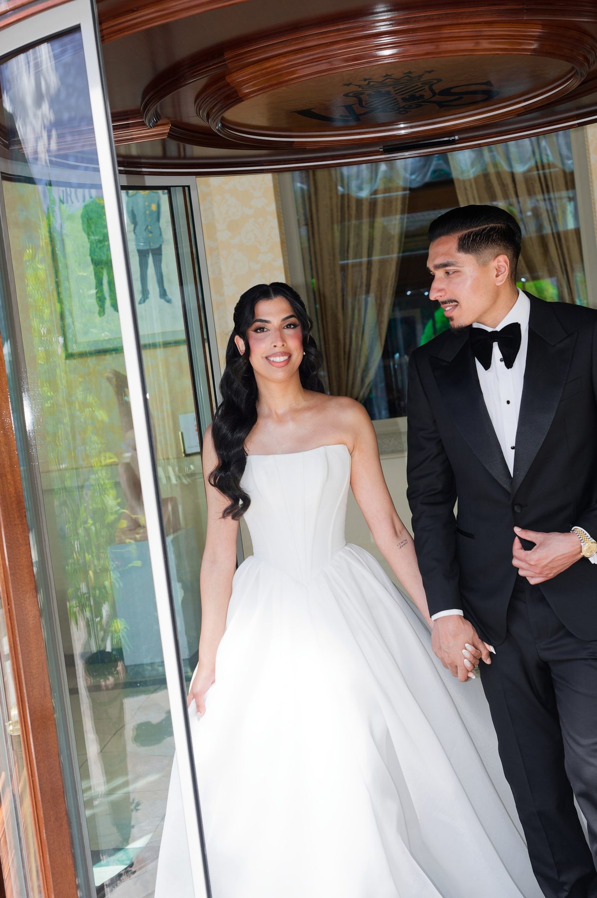 The bride and groom stepping through the hotel doors, the groom in a black custom tuxedo