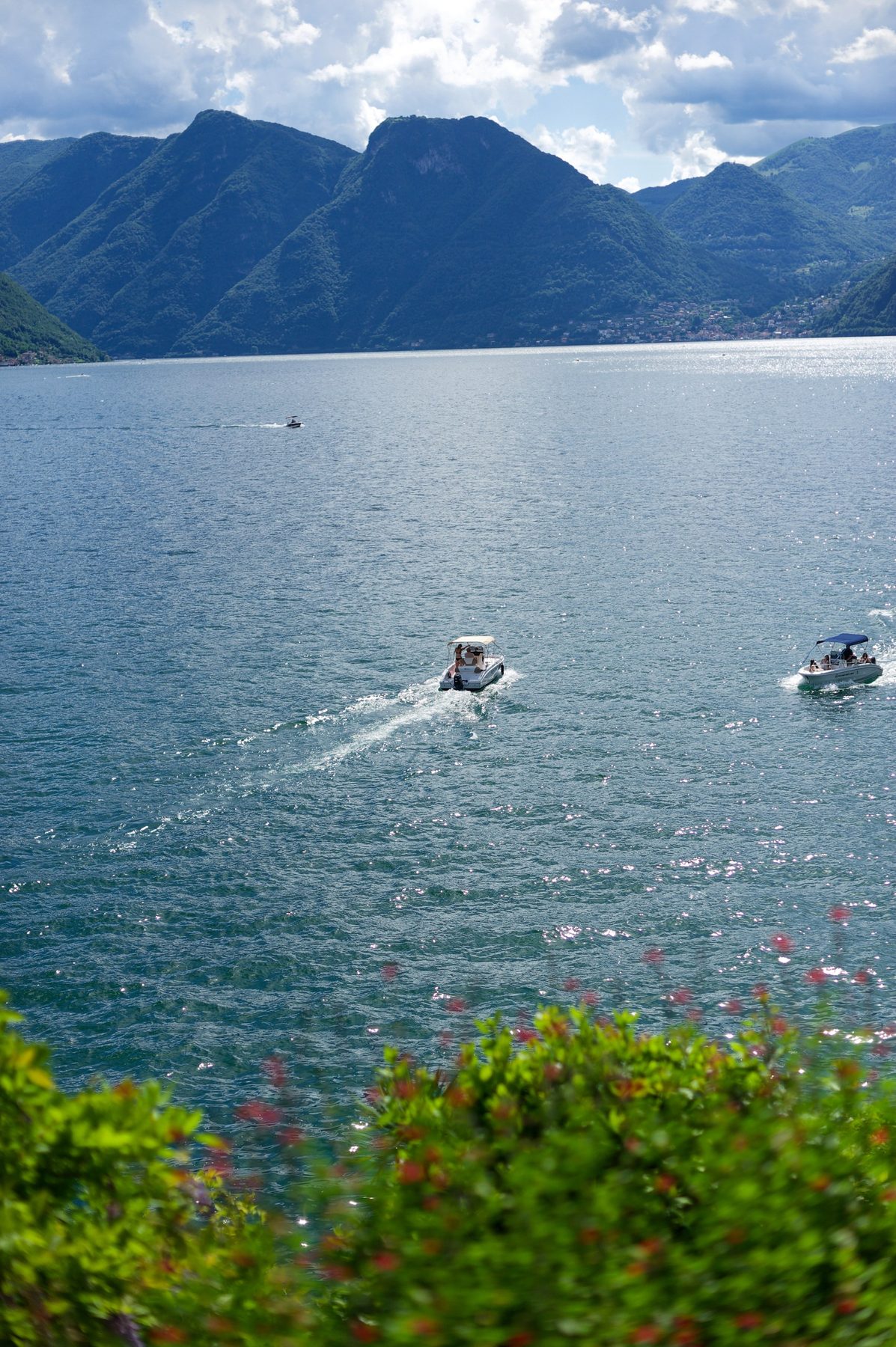 Boats crossing Lake Como below the mountains, seen from a villa garden