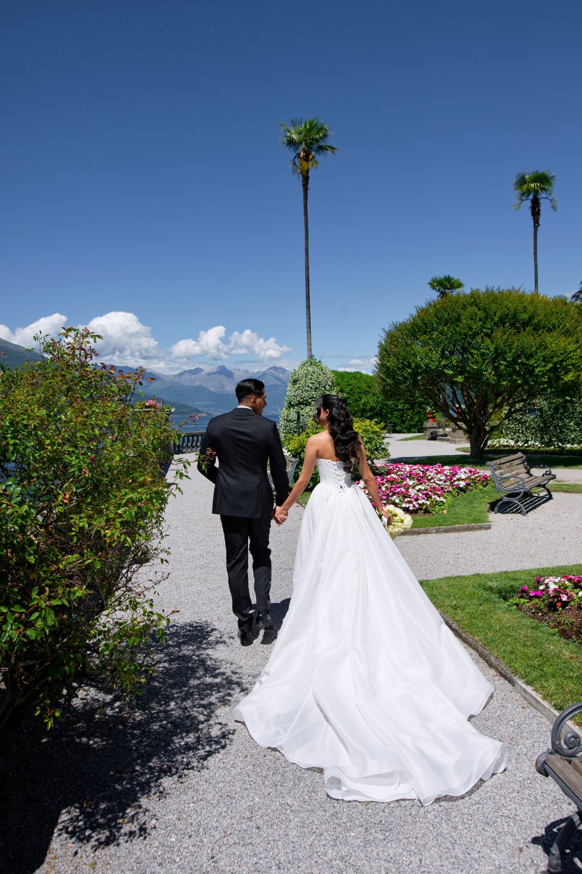 The couple walking a gravel path through a garden of palms and roses