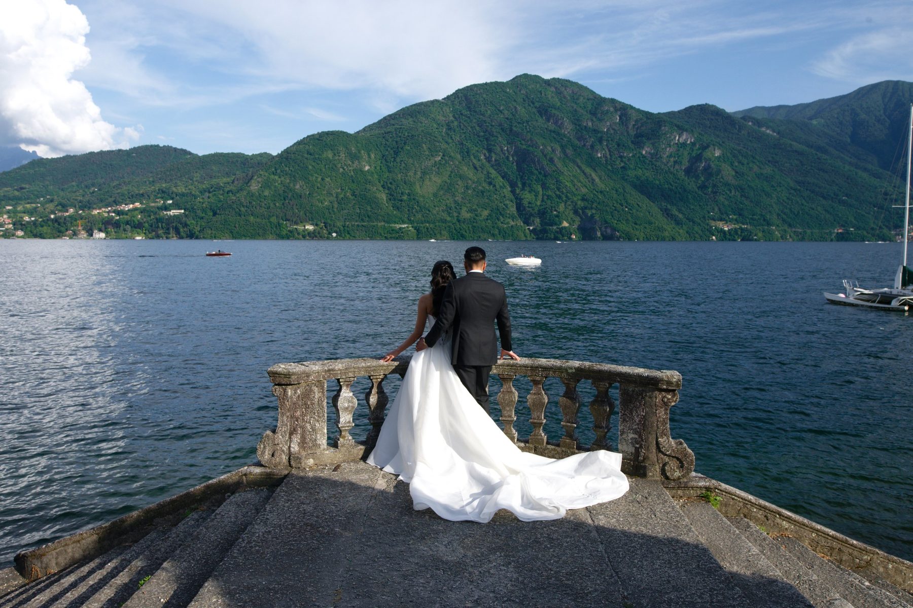 The bride and groom on a stone pier looking out over Lake Como