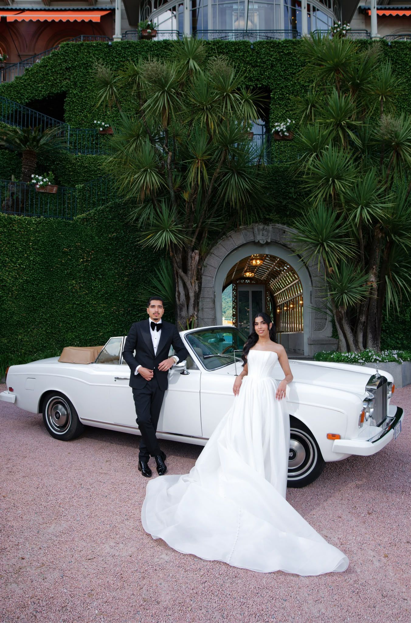 The bride and groom beside a white Rolls-Royce under the ivy-covered villa arch