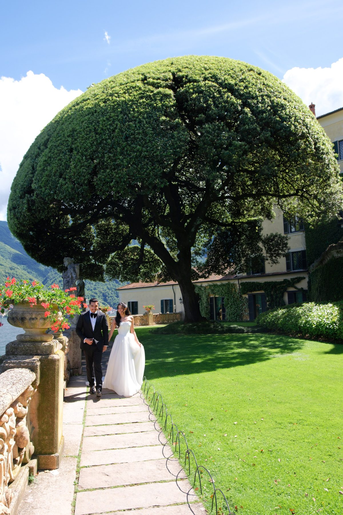 The couple walking beneath a great clipped topiary in the villa gardens
