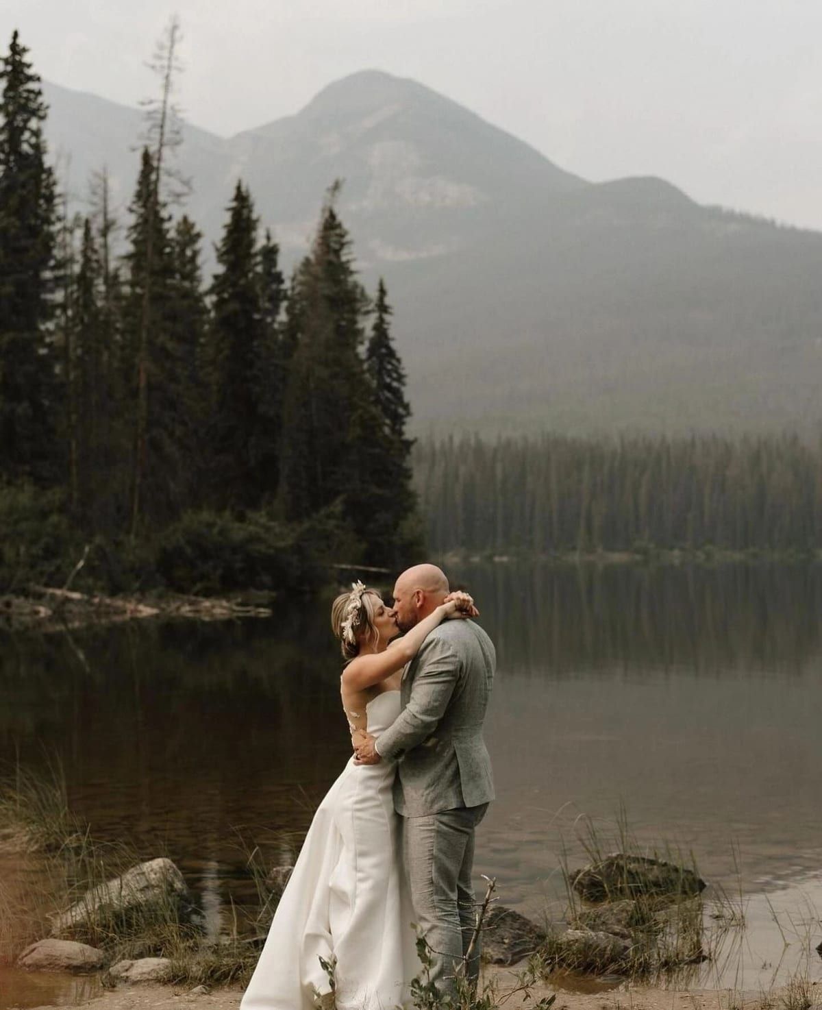 Couple embracing beside a mountain lake, wedding tailoring from Edmonton